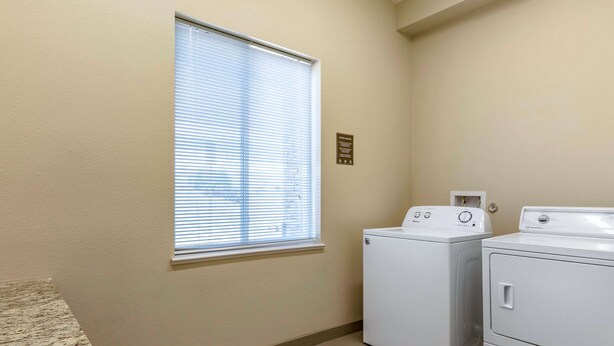 A laundry room with two white washing machines, a window with blinds, and a sign on the wall. - Comfort Inn & Suites Edgewood (Edgewood)