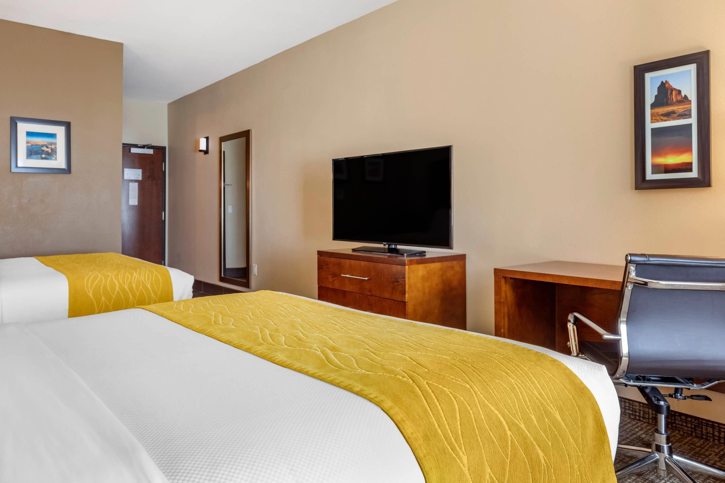 A hotel room with two beds, a television, a desk, and a chair.