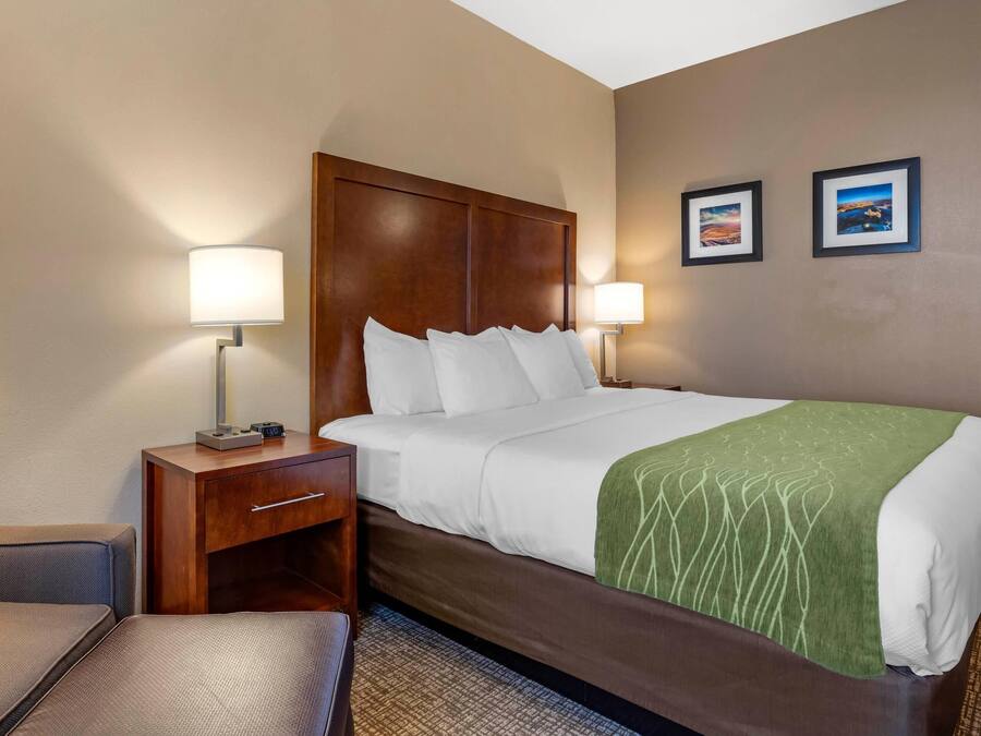 Ein Hotelzimmer mit einem Bett, zwei Nachttischlampen, einem Nachttisch, einem Sessel und zwei gerahmten Bildern an der Wand.