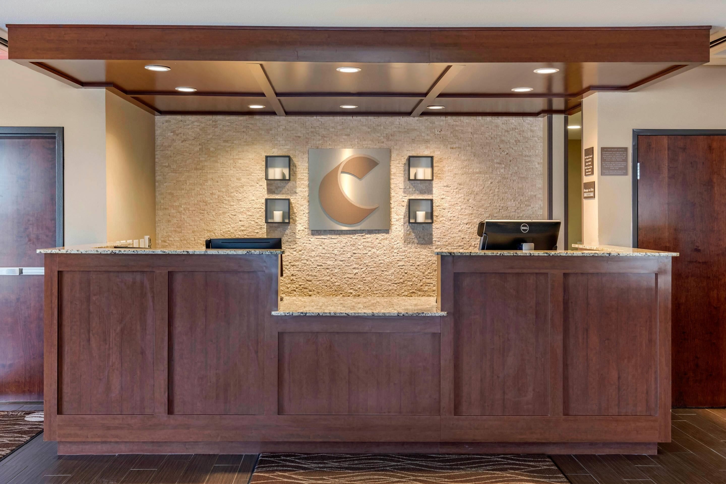 A reception desk with a stone wall backdrop, two framed wall art pieces, and a Dell computer monitor.