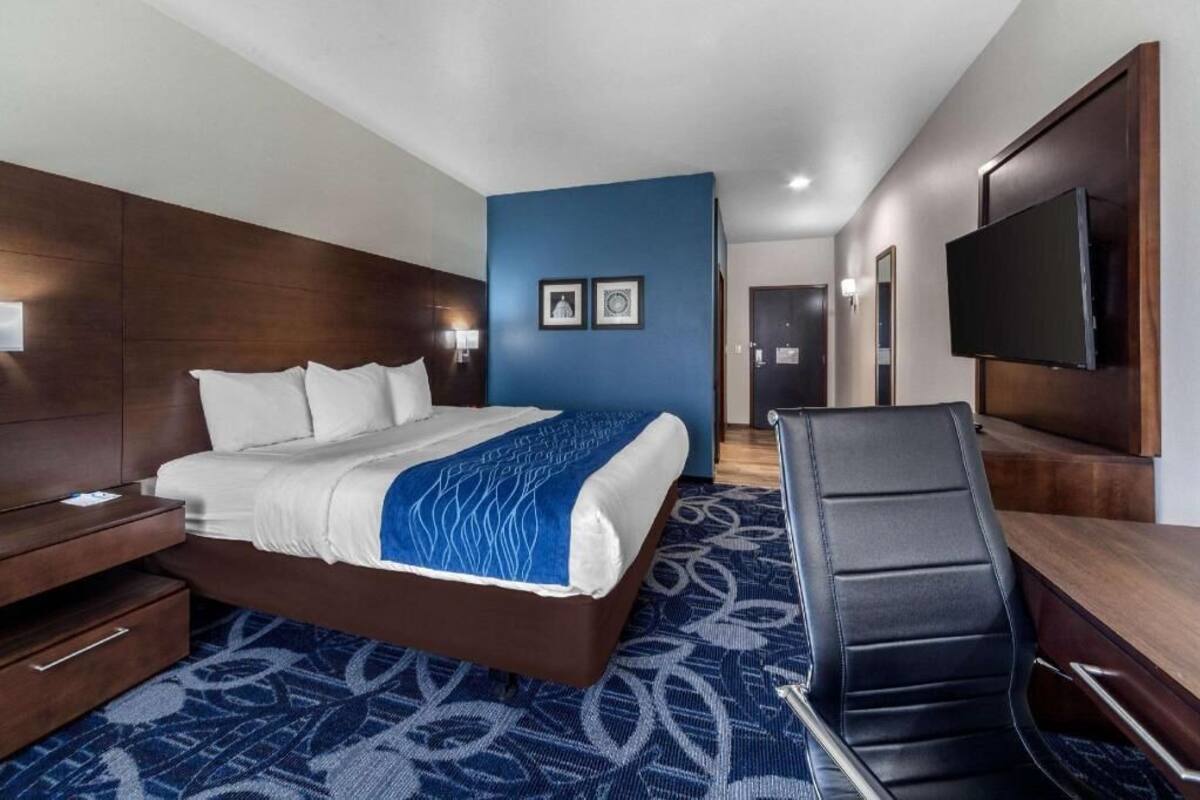 A hotel room with a bed, a desk, a chair, a TV, and a wall-mounted TV.