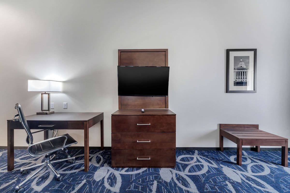 A hotel room with a desk, chair, dresser, TV, and framed picture on the wall.