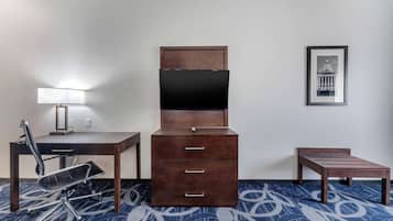 A hotel room with a desk, chair, dresser, TV, and framed picture on the wall.