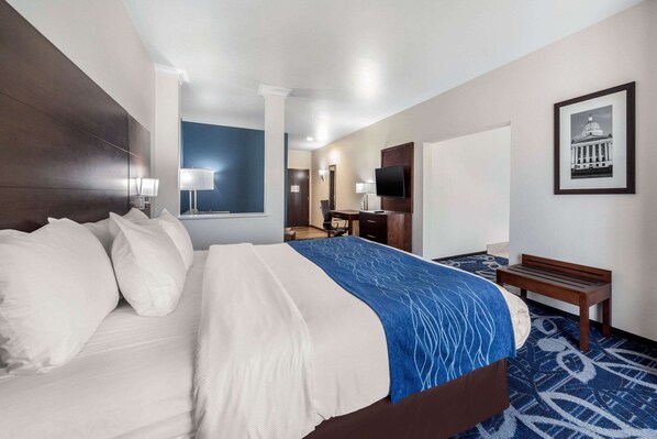 Habitación de hotel con una cama grande, un escritorio con una silla, un televisor y un cuadro en la pared.