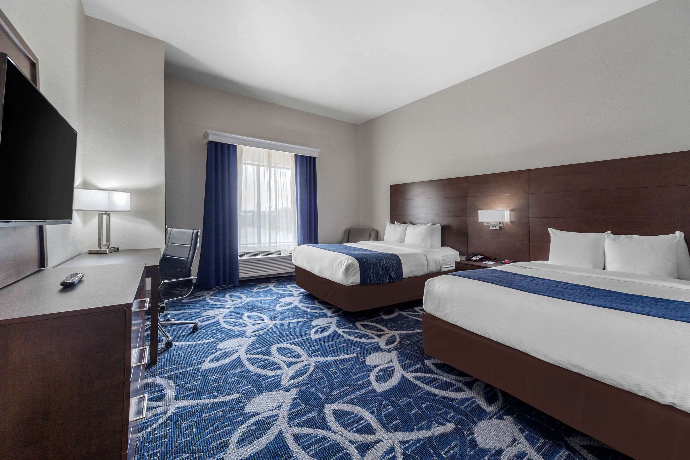 A hotel room with two beds, a desk with a TV, and a window with curtains.