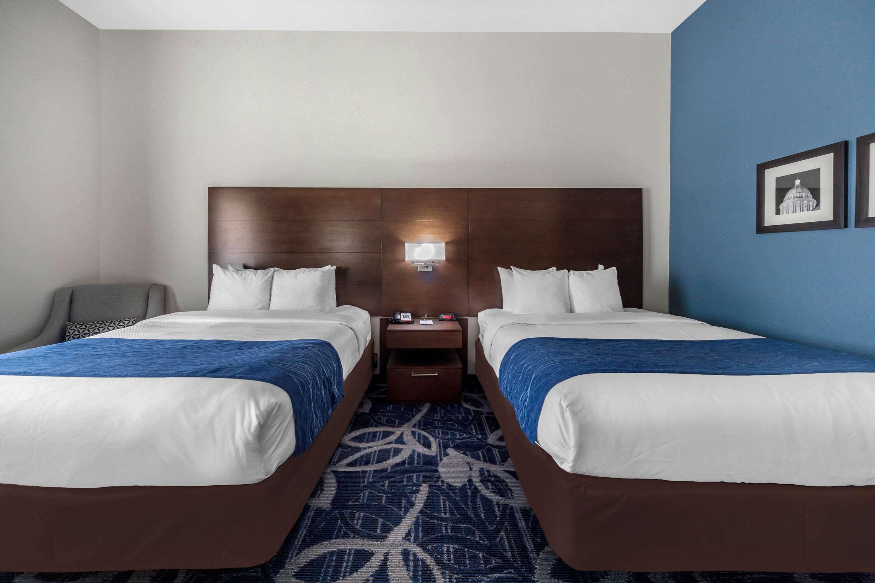 A hotel room with two beds, a nightstand, a lamp, and a wall with framed pictures.