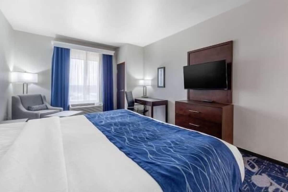 A hotel room with a bed, a desk, a chair, a TV, and a window with curtains.