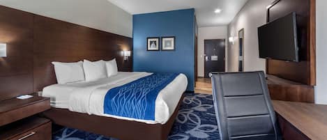 A hotel room with a bed, a desk, a chair, a TV, and a wall-mounted TV.