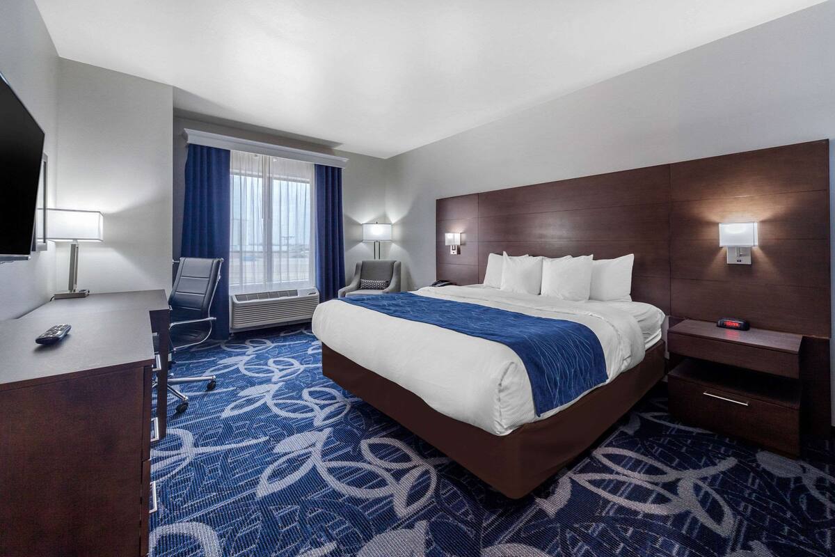 A hotel room with a large bed, a desk with a chair, a television, and a window with curtains.