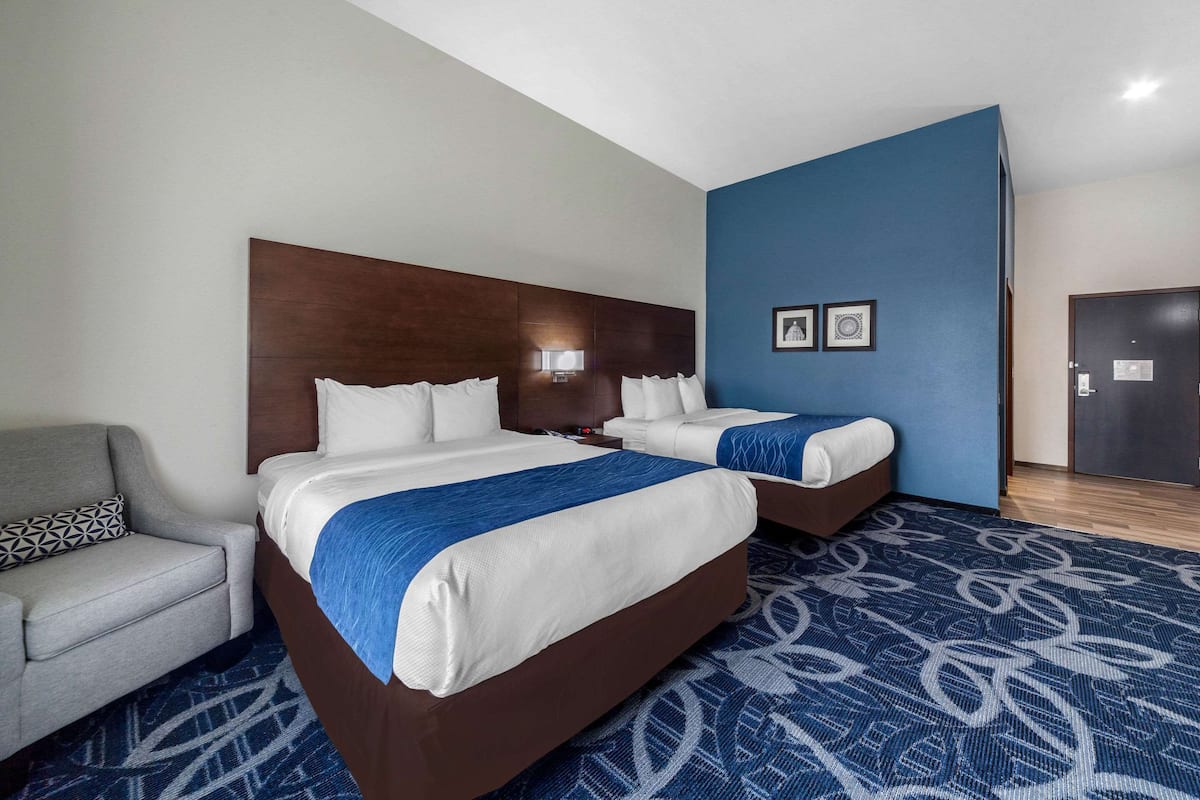 A hotel room with two beds, a sofa, and a patterned carpet.