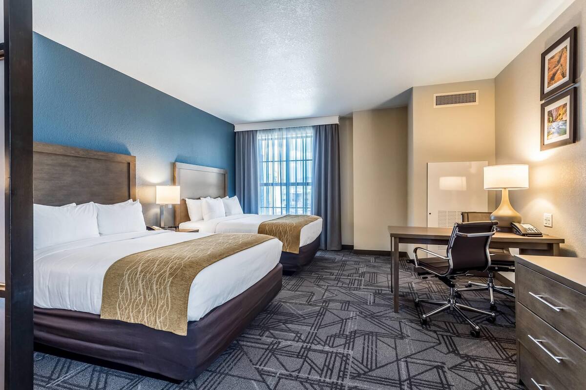 Une chambre d’hôtel avec deux lits, un bureau, une chaise et une commode.