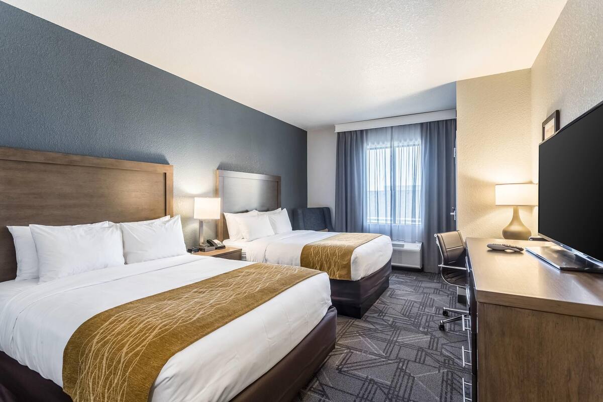 Une chambre d’hôtel avec deux lits, un bureau, une chaise, une télévision et une fenêtre avec des rideaux.