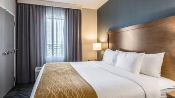 A hotel room with a large bed, a headboard, a nightstand with a lamp, and a window with curtains.