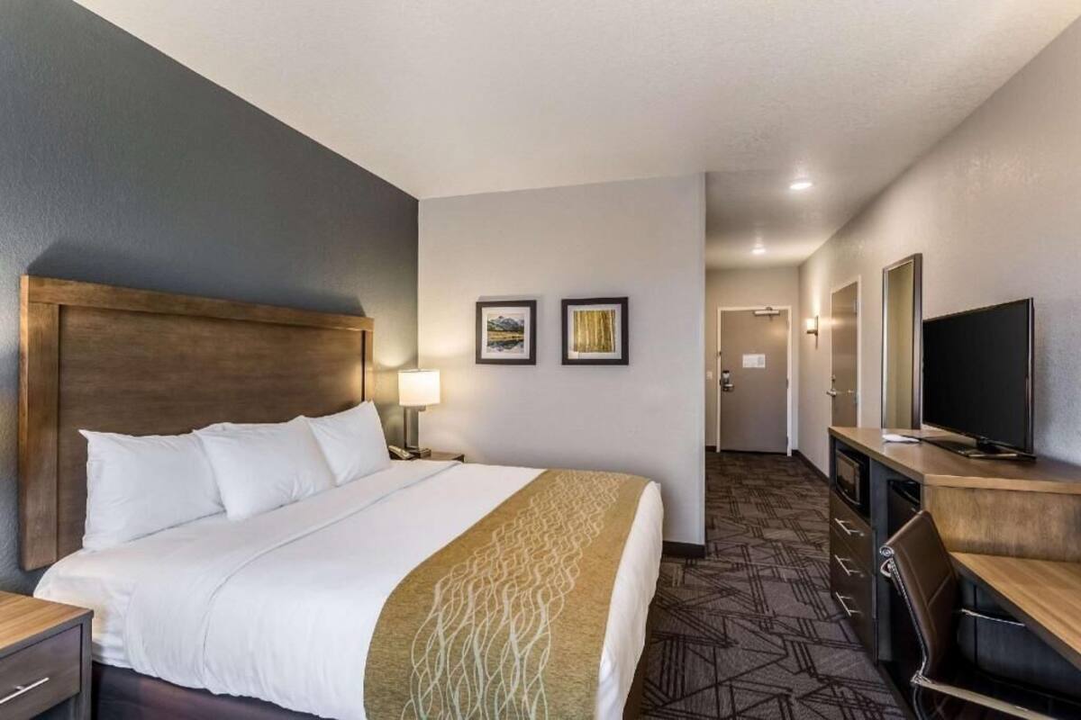 Une chambre d’hôtel avec un grand lit, un bureau, une télévision et une porte donnant sur un couloir.