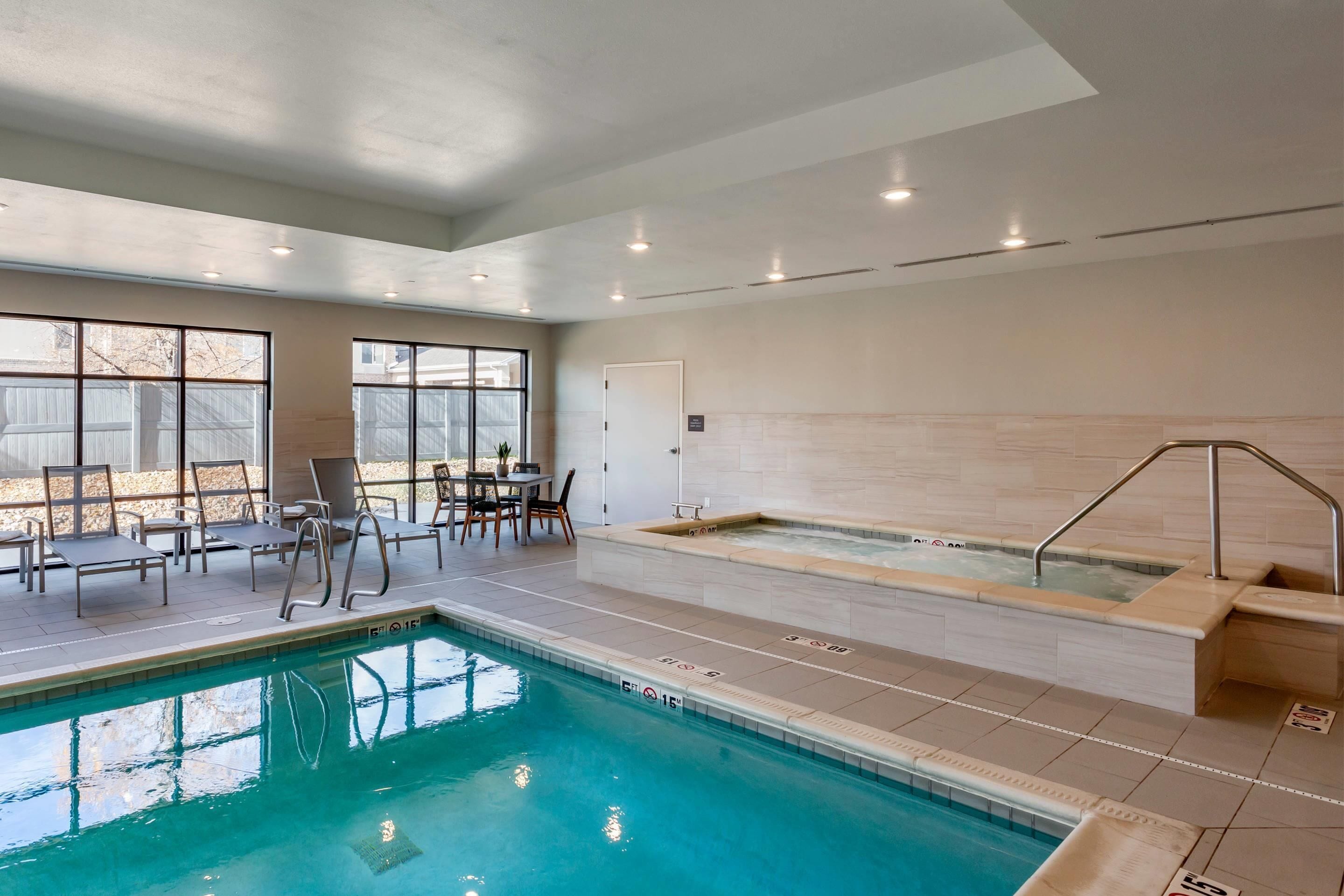 An indoor swimming pool with a hot tub, lounge chairs, and a sunlit patio area.