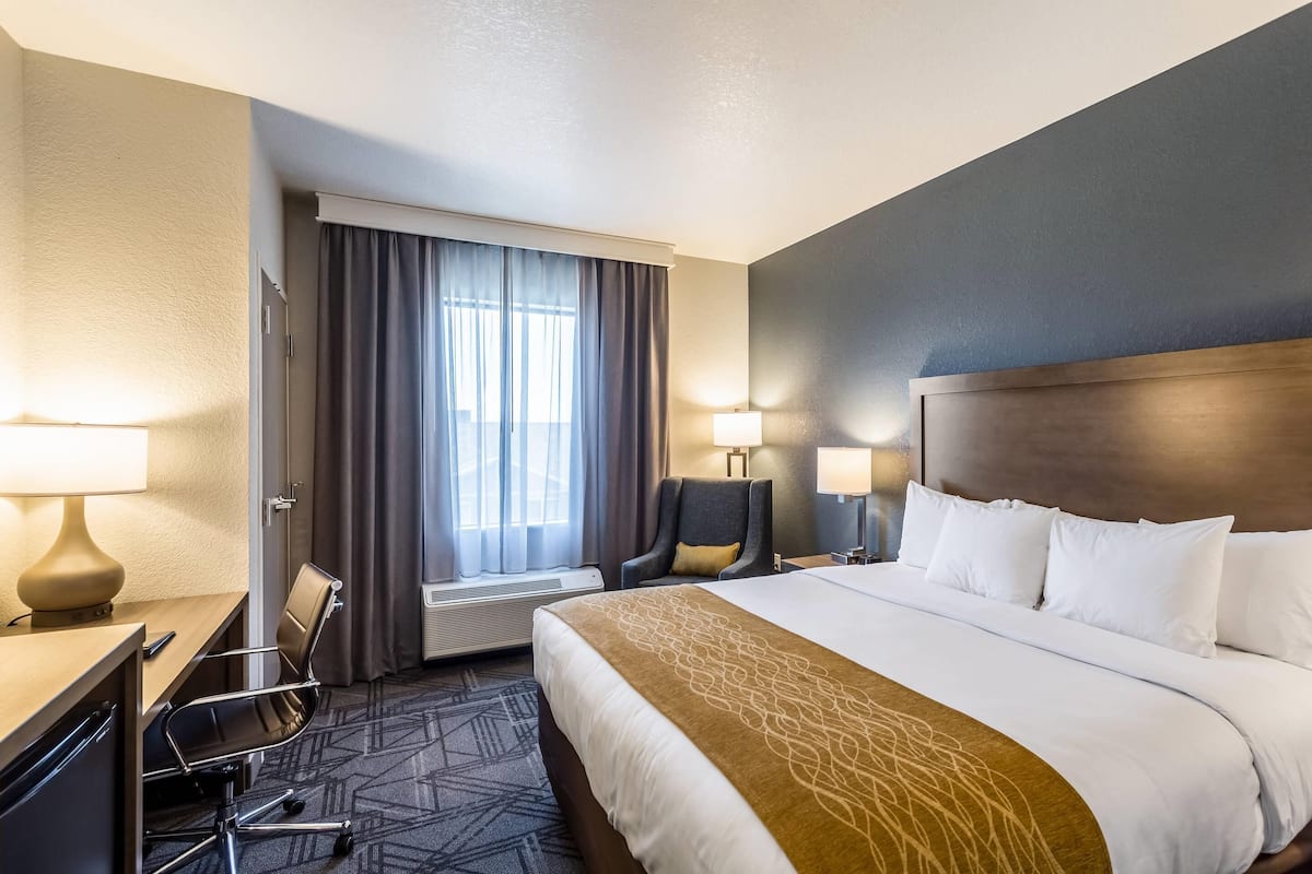 Une chambre d’hôtel avec un grand lit, un bureau avec une chaise, une fenêtre avec des rideaux et deux lampes de chevet.