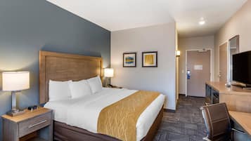A hotel room with a large bed, bedside tables, a desk with a chair, a television, and two framed pictures on the wall.