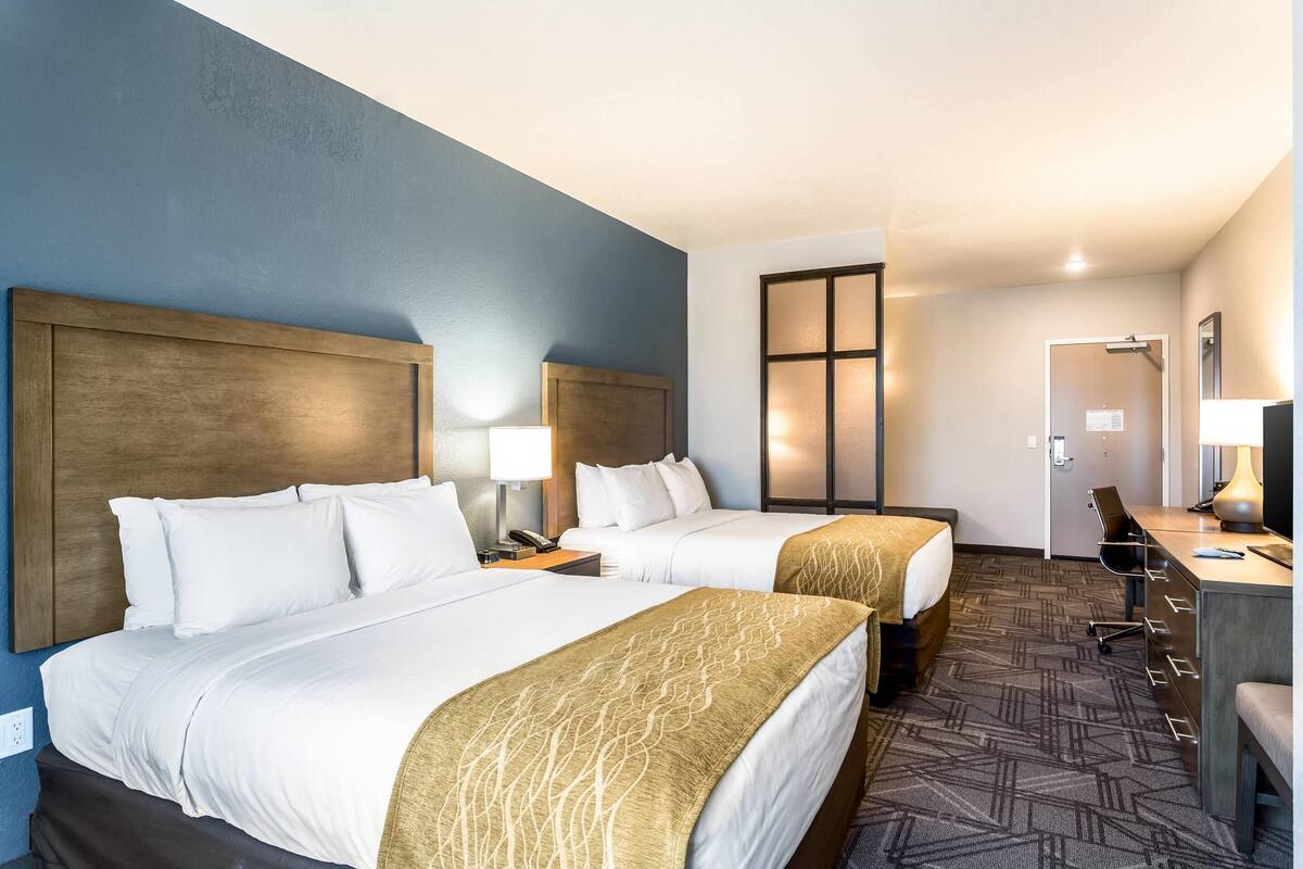 Une chambre d’hôtel avec deux lits, un bureau, une chaise et une porte.