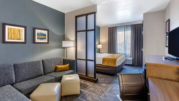 Een hotelkamer met een bank, voetenbankje, bed, bureau en televisie.