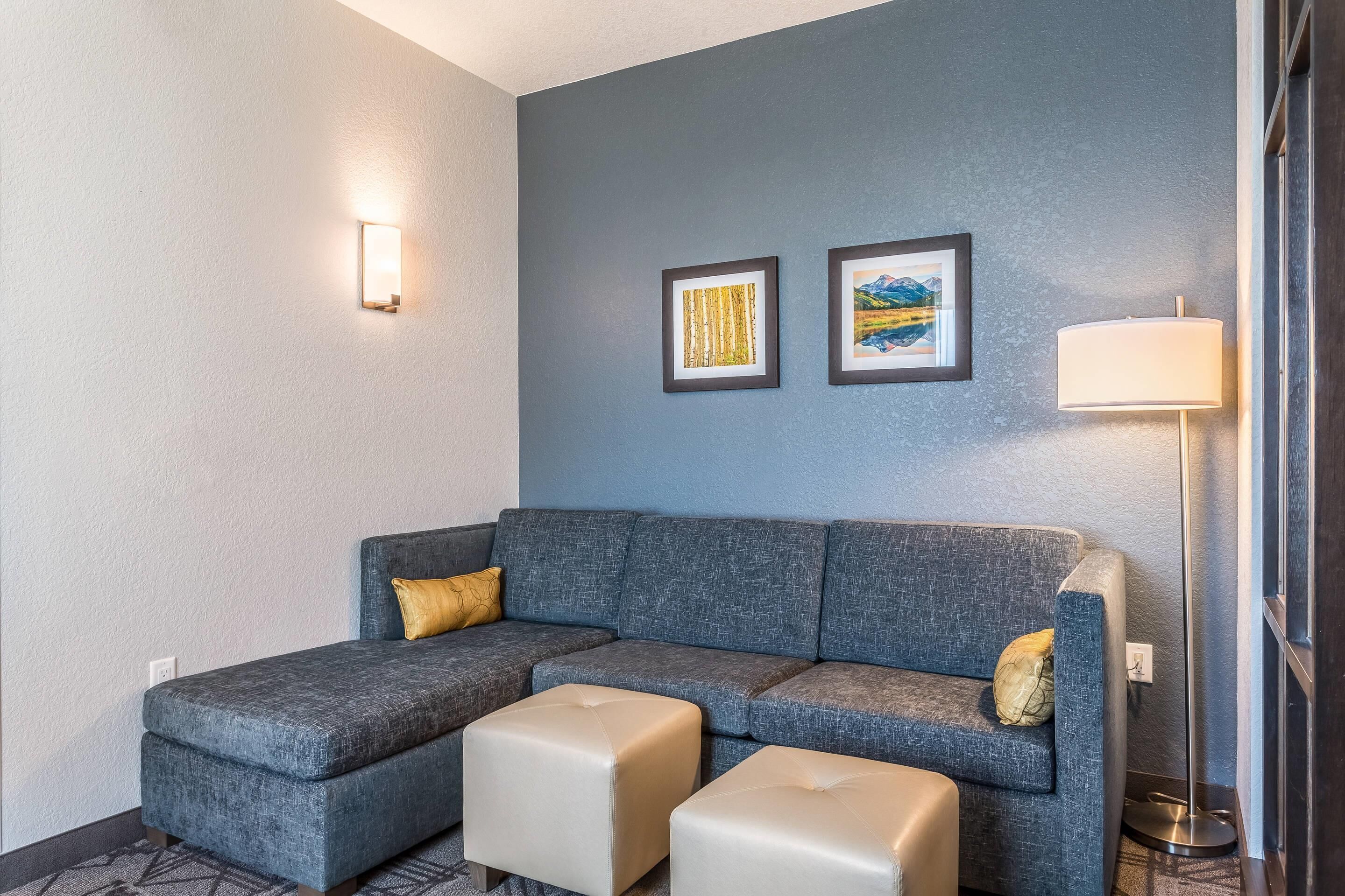 A modern living room with a grey sectional sofa, two ottomans, a floor lamp, and two framed pictures on the wall.