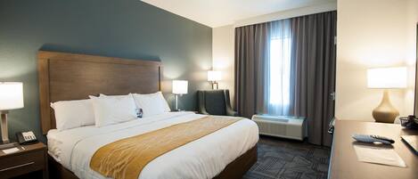 Habitación de hotel con una cama grande, lámparas de noche, un escritorio con lámpara y una ventana con cortinas.