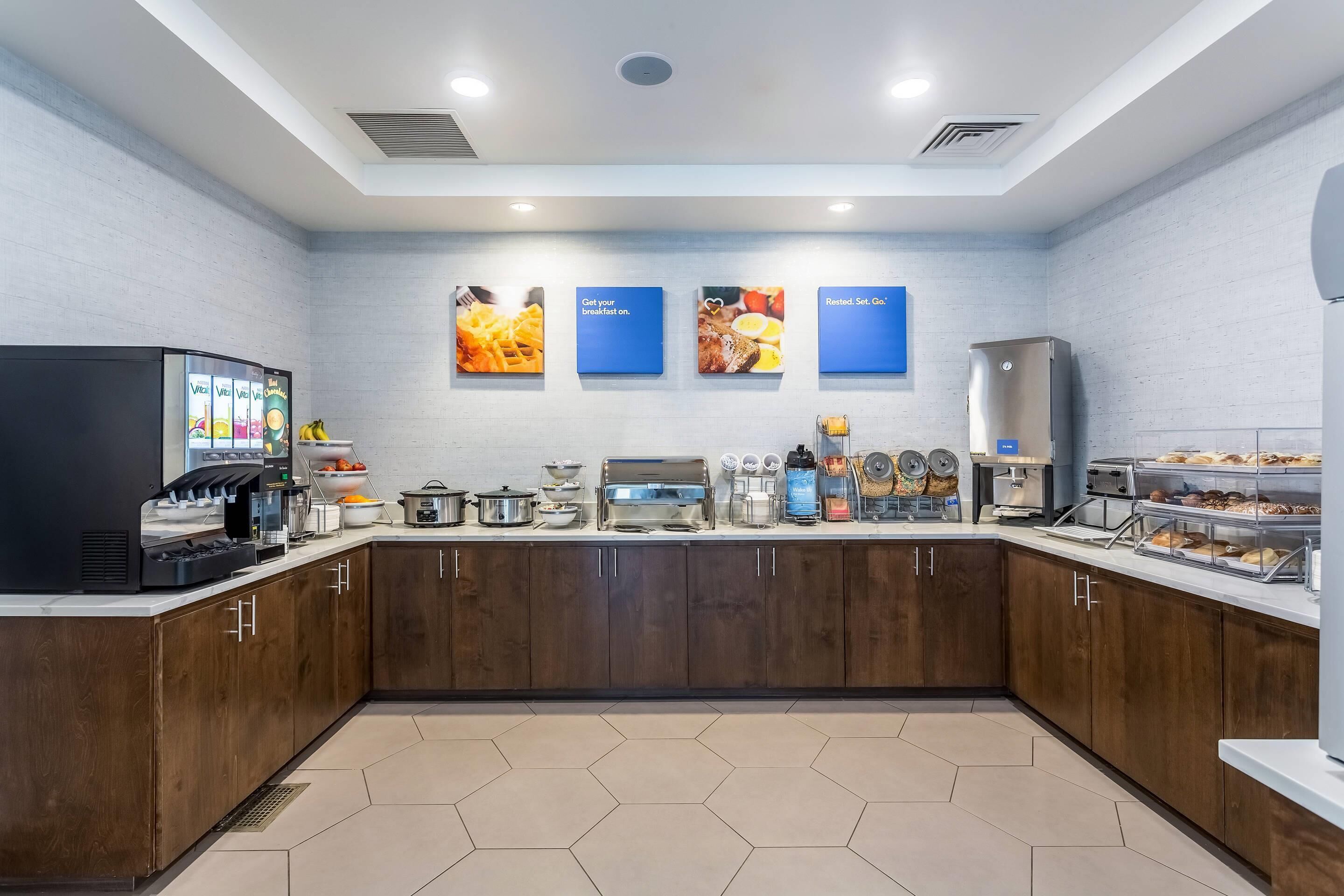 A modern breakfast area with a coffee machine, food display, and a microwave.
