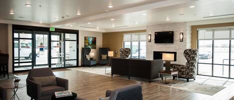 A spacious lobby with a reception desk, comfortable seating, a fireplace, and large windows offering views of the parking area.