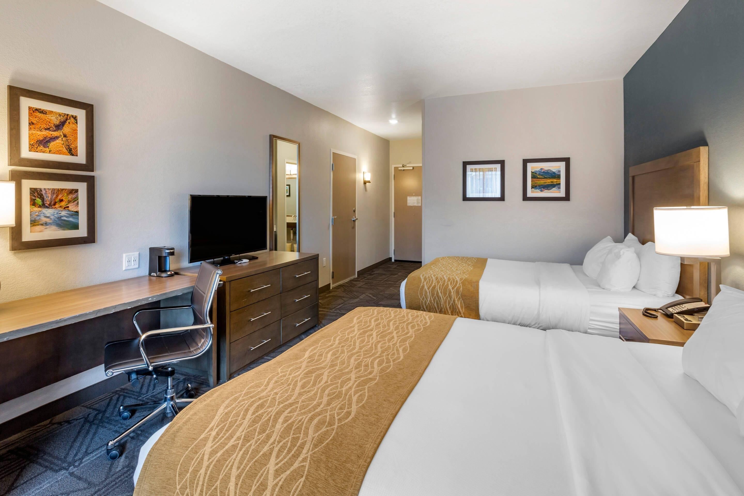 Una habitación de hotel con cama, escritorio con silla, televisión y obras de arte en las paredes.