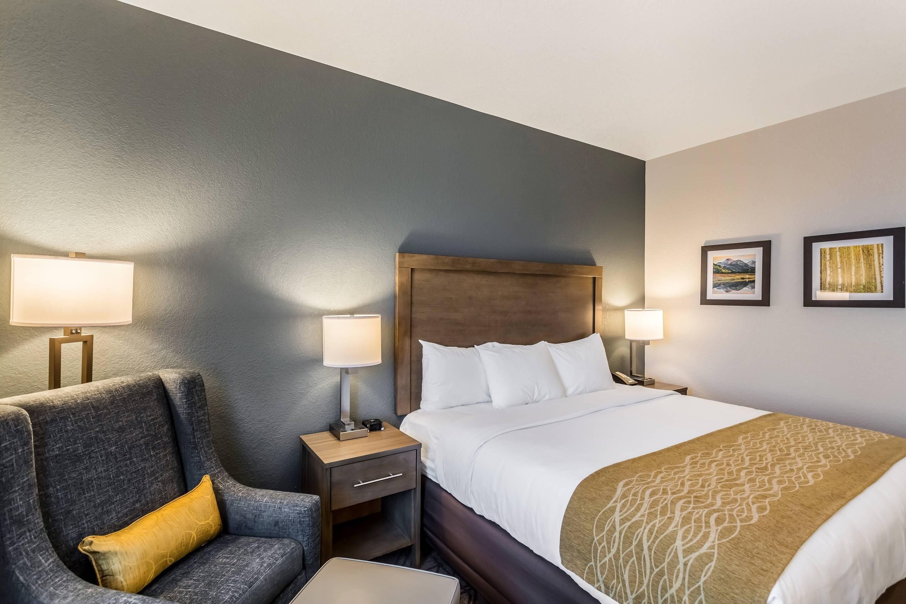 Une chambre d’hôtel comprenant un lit, une chaise, une table de chevet et deux lampes fixées au mur.