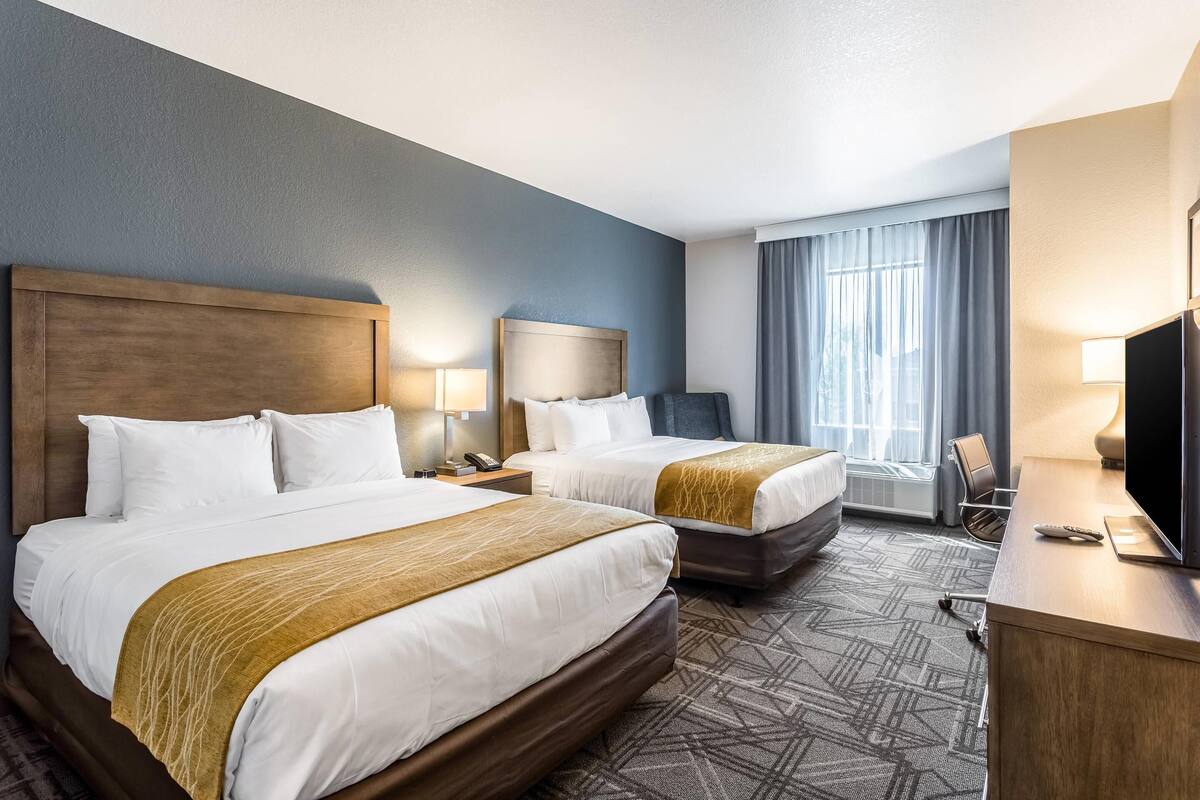 Une chambre d’hôtel avec deux lits, un bureau avec une télévision et une fenêtre avec des rideaux.