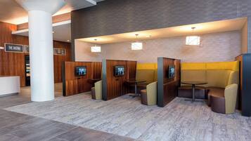 Un hall d’hôtel moderne avec un comptoir d’accueil, une enseigne de bistro, des espaces salon et une grande colonne.
