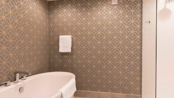 A bathroom with a geometric patterned wall, a white bathtub, and a glass shower enclosure.