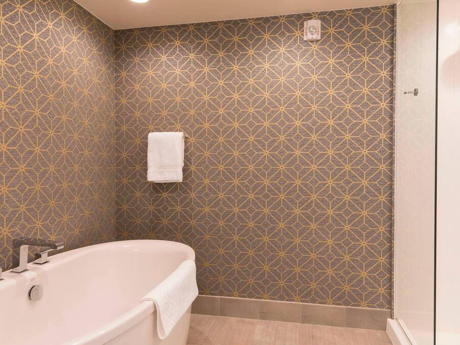 A bathroom with a geometric patterned wall, a white bathtub, and a glass shower enclosure.