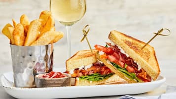 A plate with a grilled sandwich, a glass of white wine, and a container of fries.
