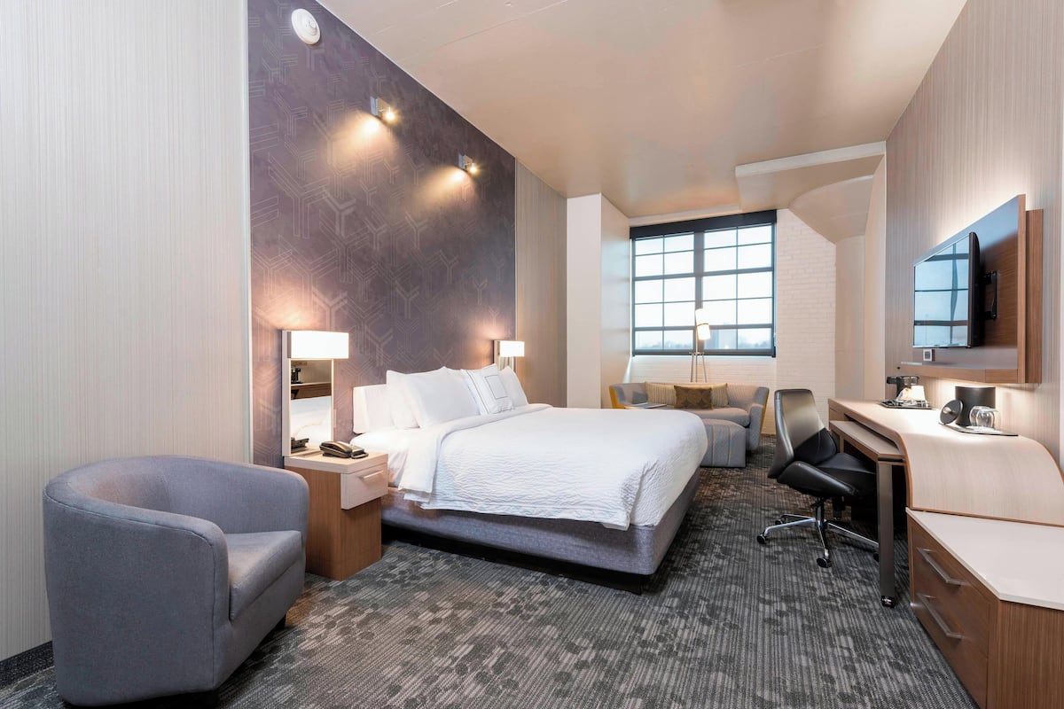 A modern hotel room with a large bed, a desk, a chair, a TV, and a window.