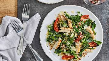 Une assiette de nourriture, avec une fourchette et un couteau posés sur une serviette, et un verre de vin rouge sur une table.