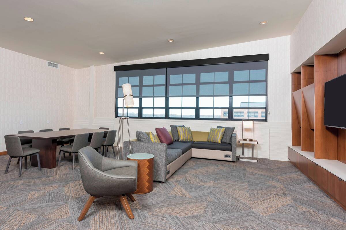 A modern conference room with a large table, chairs, a sofa, and a TV.