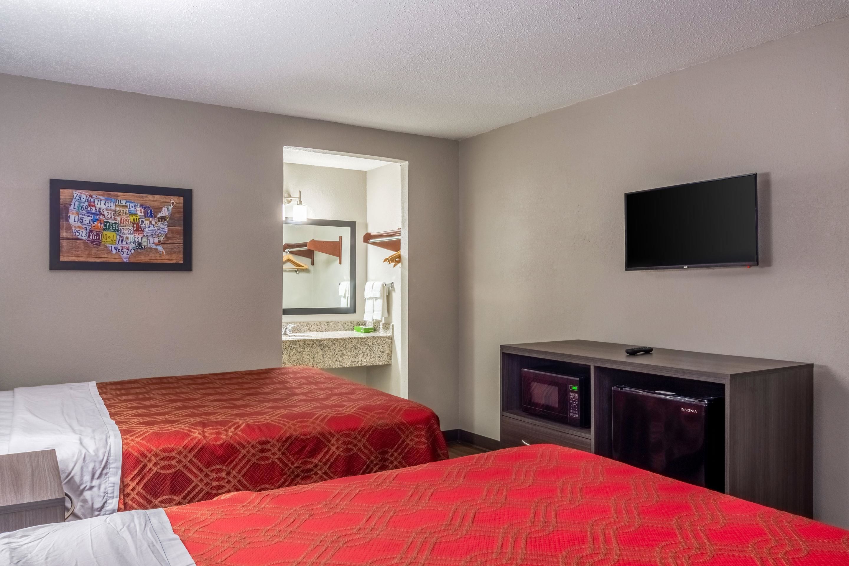 A hotel room with two beds, a television, a minibar, and a wall-mounted TV.