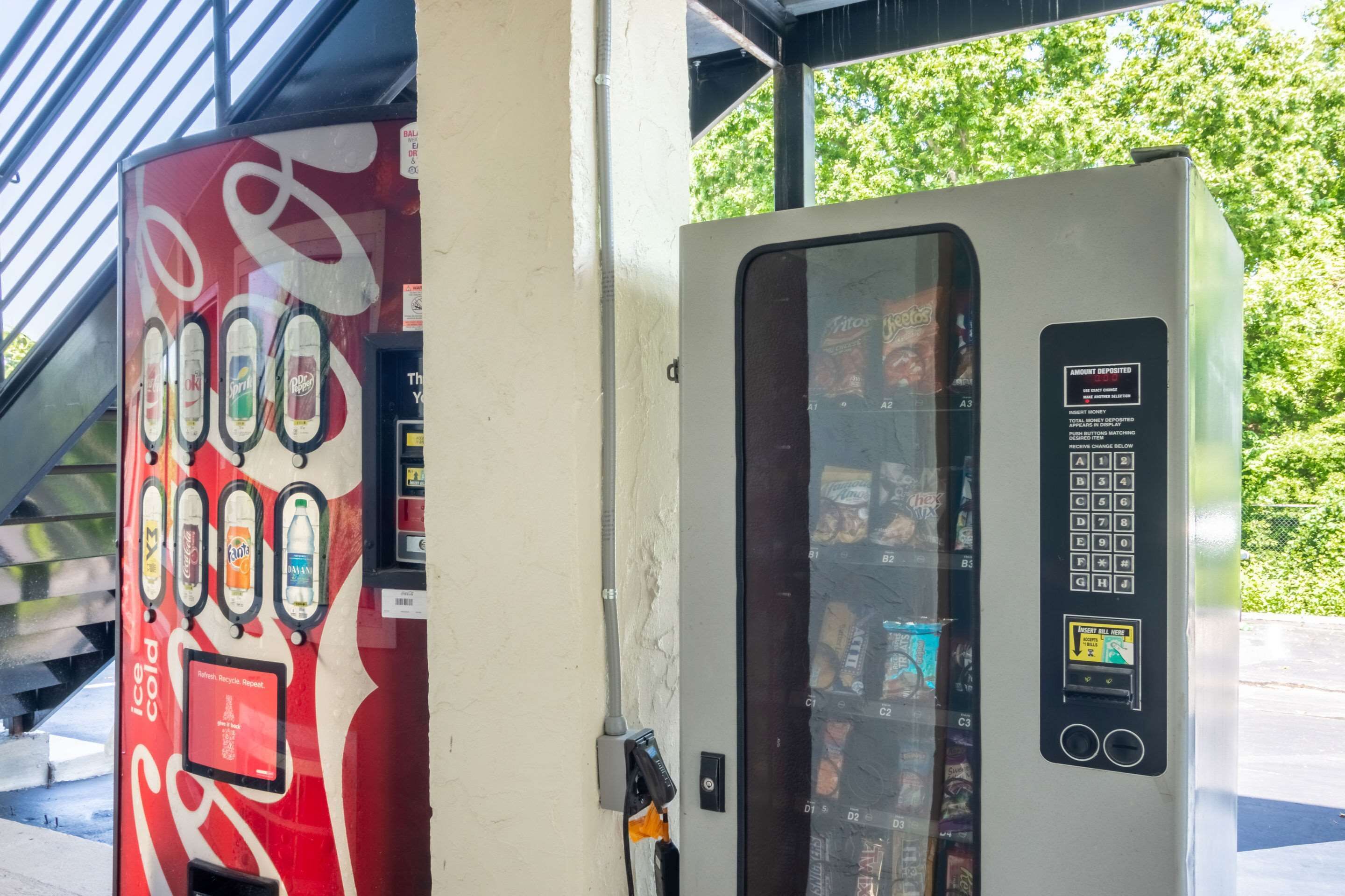 Ein Automat mit Coca-Cola-Logo und Recyclingzeichen, sowie ein Automat mit Tastatur und Bildschirm.