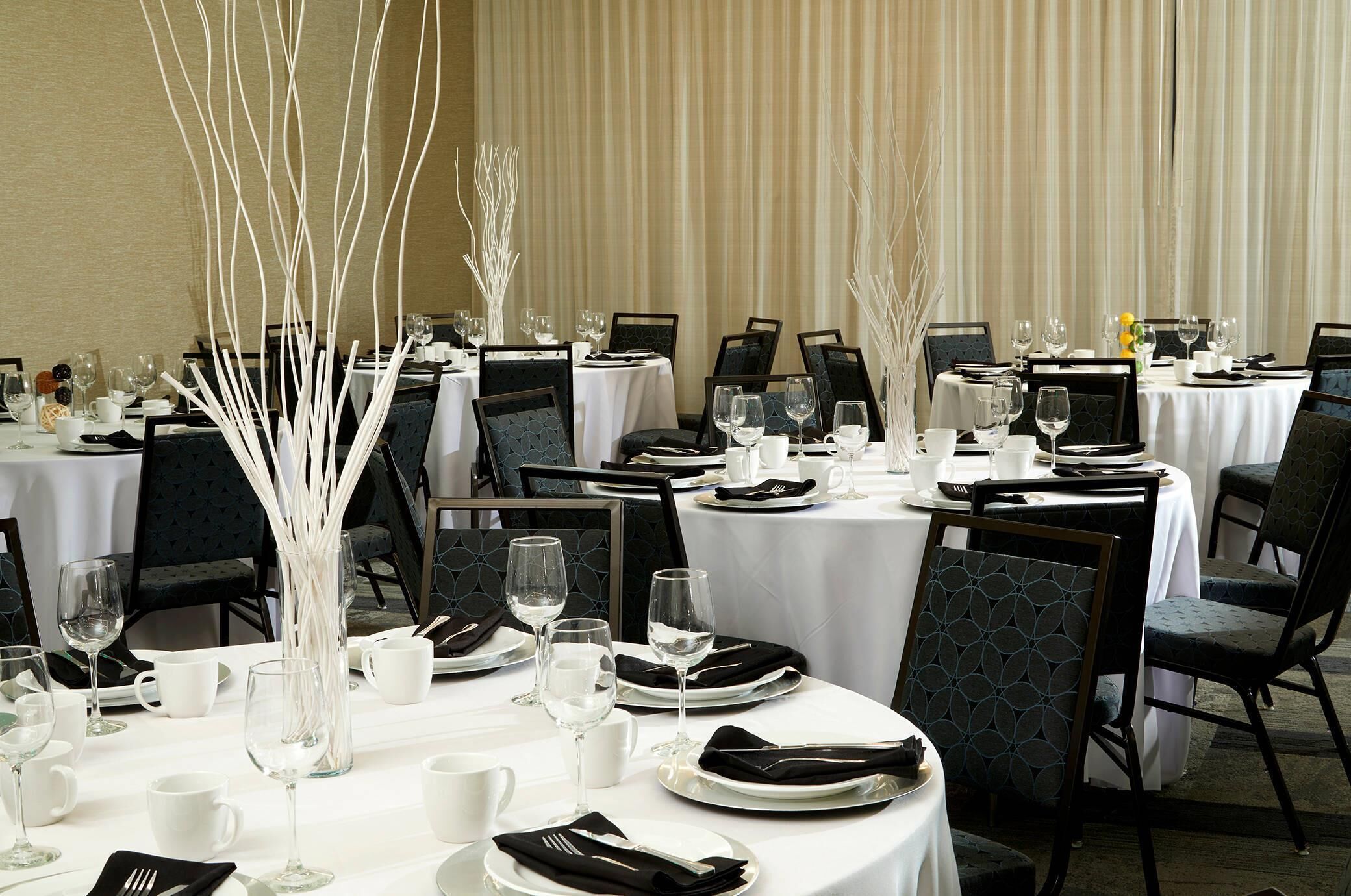 A dining area with round tables, black chairs, white tablecloths, and white decorative vases.