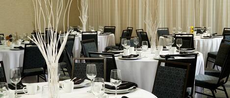 A dining area with round tables, black chairs, white tablecloths, and white decorative vases.