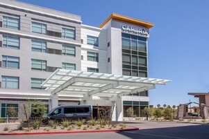 Un edificio de hotel moderno con un llamativo letrero 'CAMBRIA', un acceso cubierto y un estacionamiento con una camioneta identificada con 'CAMBRIA'.