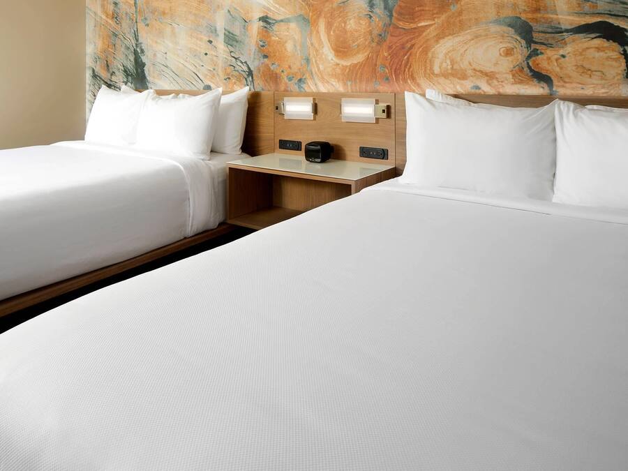 A hotel room with two beds, a wooden headboard, bedside tables with lamps, and a large abstract painting on the wall.