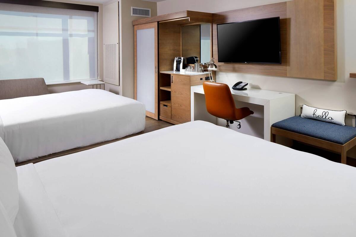Une chambre d’hôtel avec deux lits, un bureau avec une chaise, une télévision et une fenêtre.