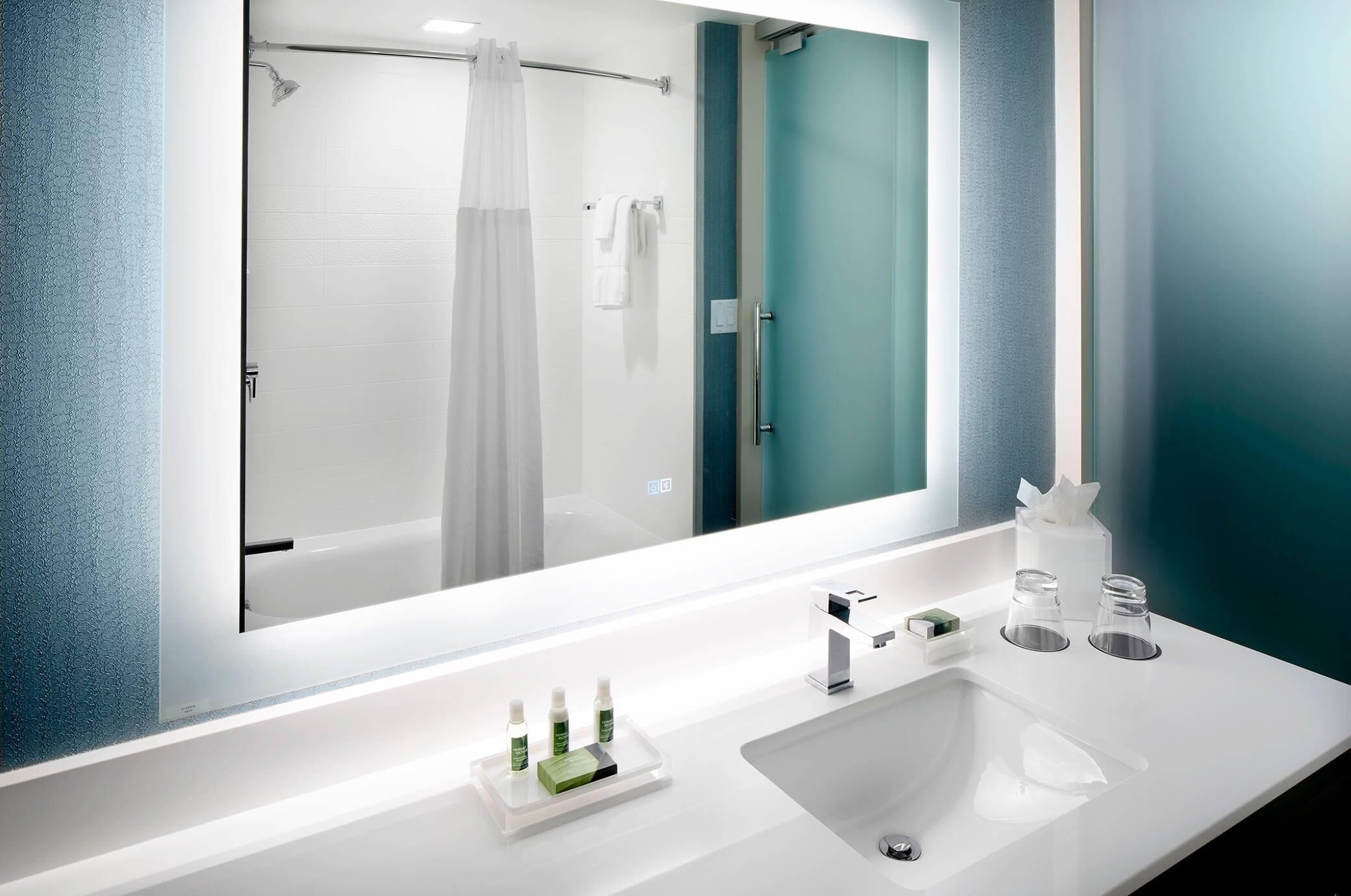 Un bany modern amb un mirall gran, una dutxa i un lavabo amb productes de tocador.