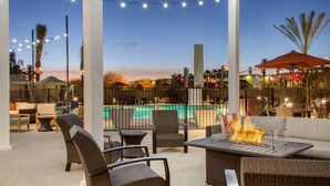 Un patio al aire libre con mobiliario de mimbre, una chimenea y vistas a una piscina.