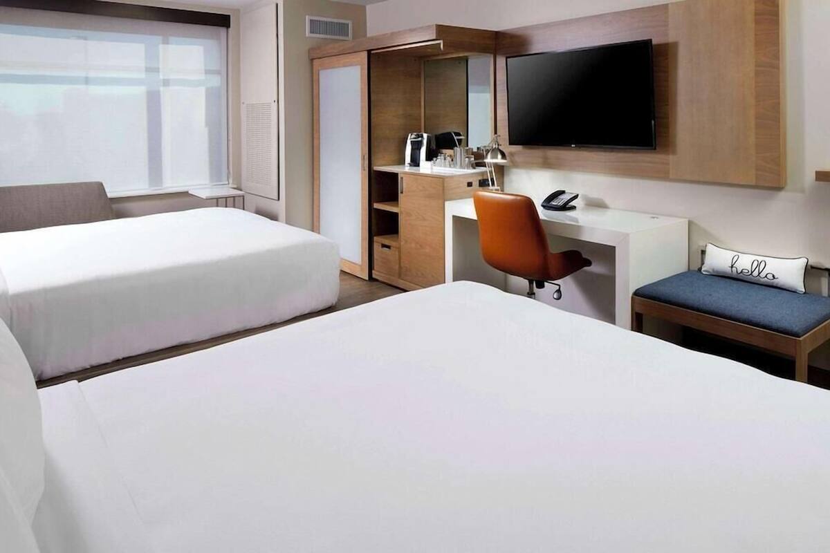 Une chambre d’hôtel avec deux lits, un bureau avec une chaise, une télévision et une armoire.