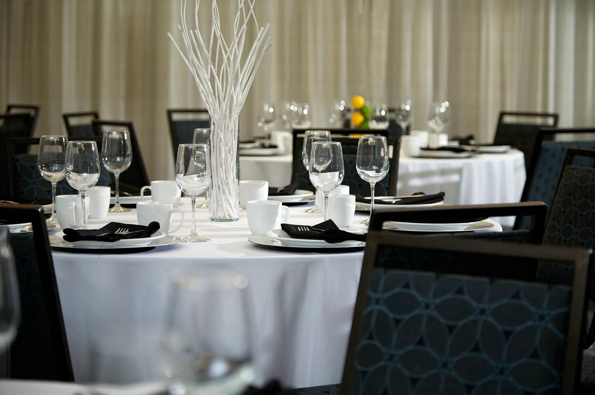 A dining table set with white tablecloths, clear glassware, and black napkins.