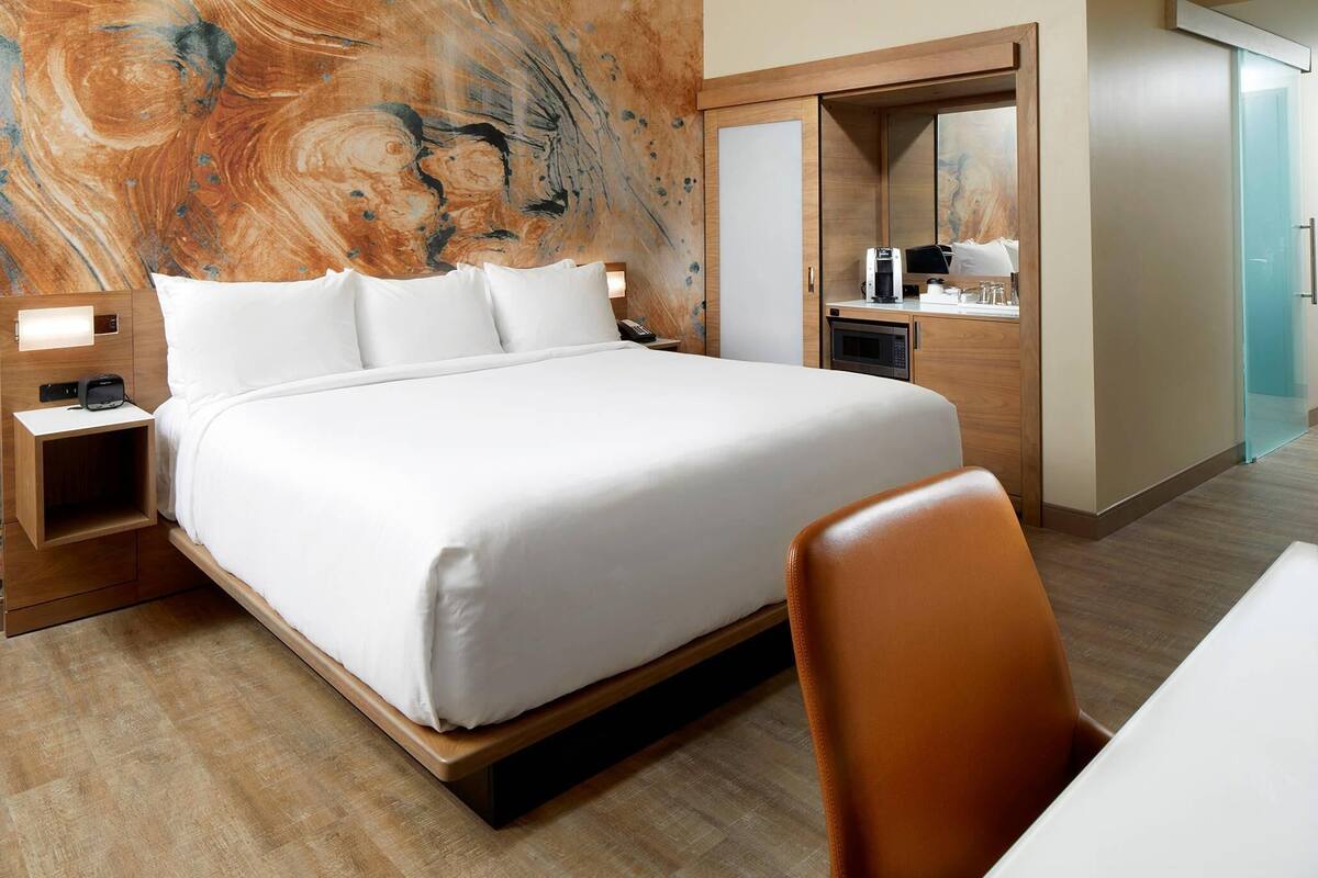 Une chambre d’hôtel avec un grand lit, un bureau avec une chaise, un miroir et un mur au motif évoquant le marbre.