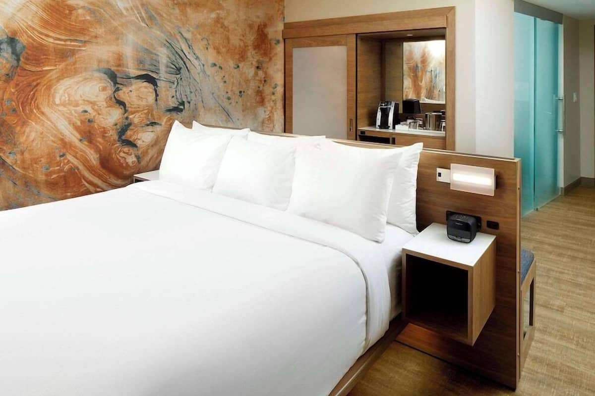 Une chambre d’hôtel avec un grand lit, une table de chevet avec une machine à café, une armoire et un mur au motif rappelant le marbre.